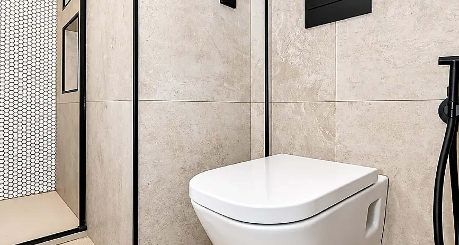Inodoro suspendido en baño reformado en calle Tarragona, Madrid, con cisterna empotrada, revestimiento beige y detalles negros.