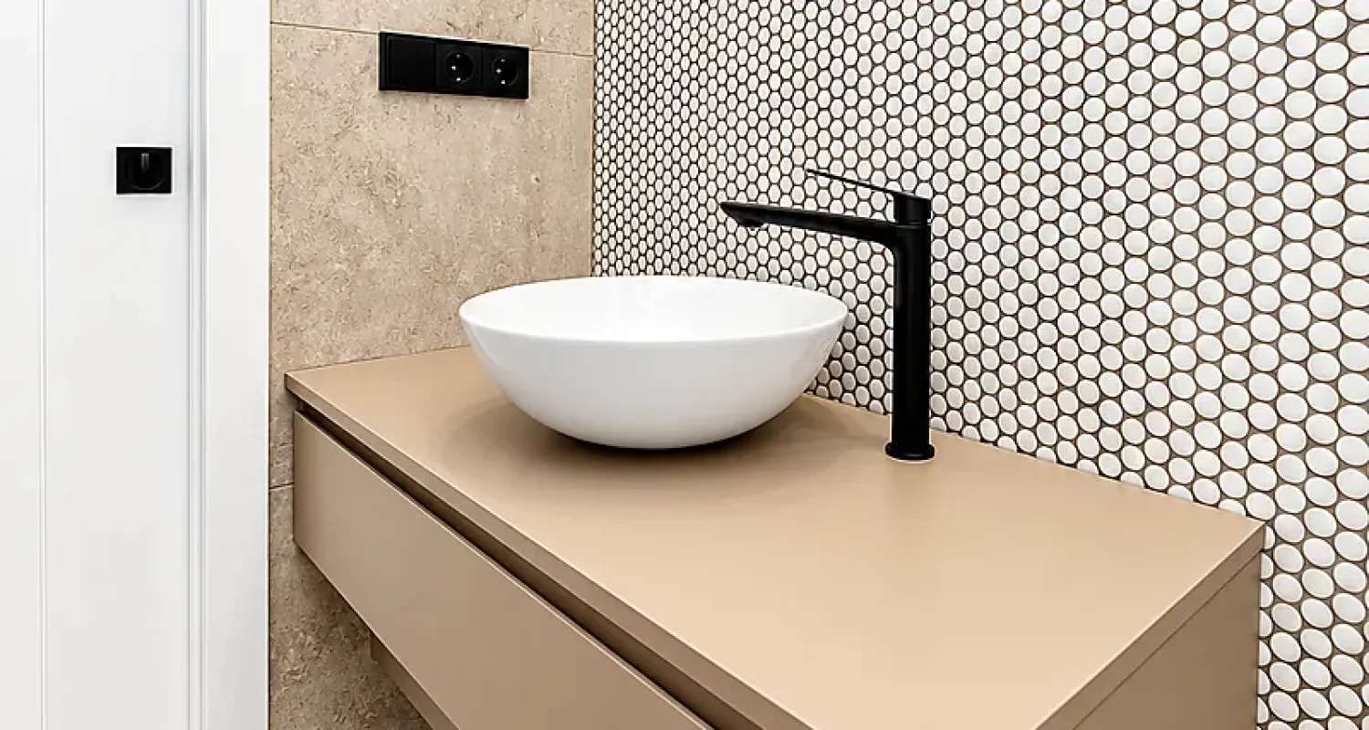 Baño reformado en calle Tarragona, Madrid, con lavabo blanco, mueble suspendido beige, grifería negra y mosaico circular.
