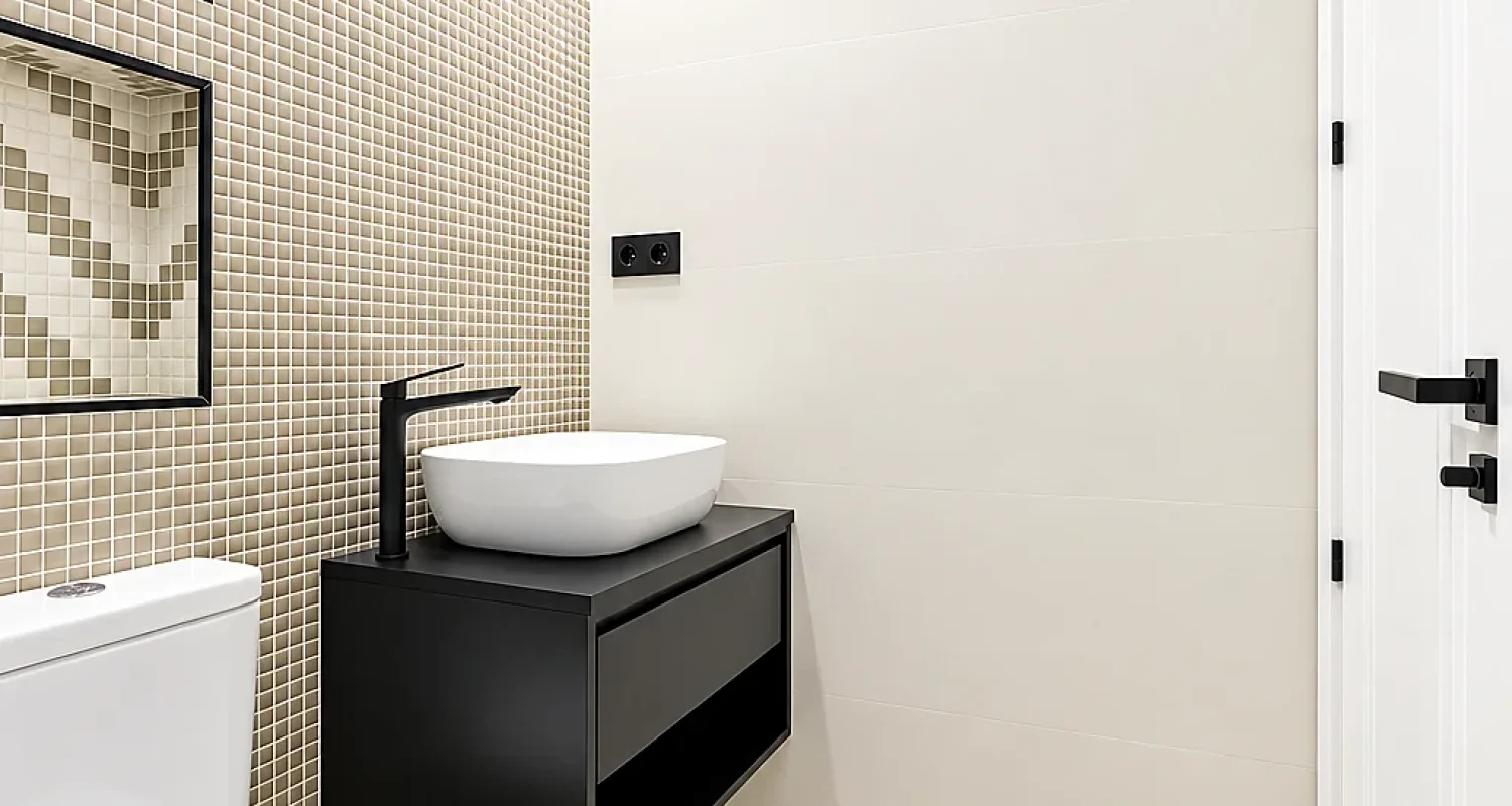 Baño reformado en calle Tarragona, Madrid, con mueble suspendido negro, lavabo blanco y suelo de mosaico geométrico.