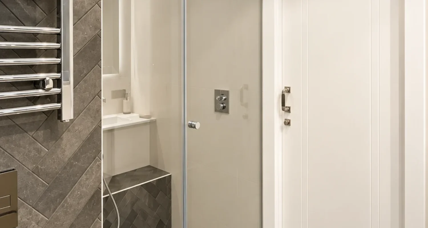 Ducha del baño principal reformado en ático de Aviador Zorita, Madrid, con mampara de cristal y revestimiento gris.