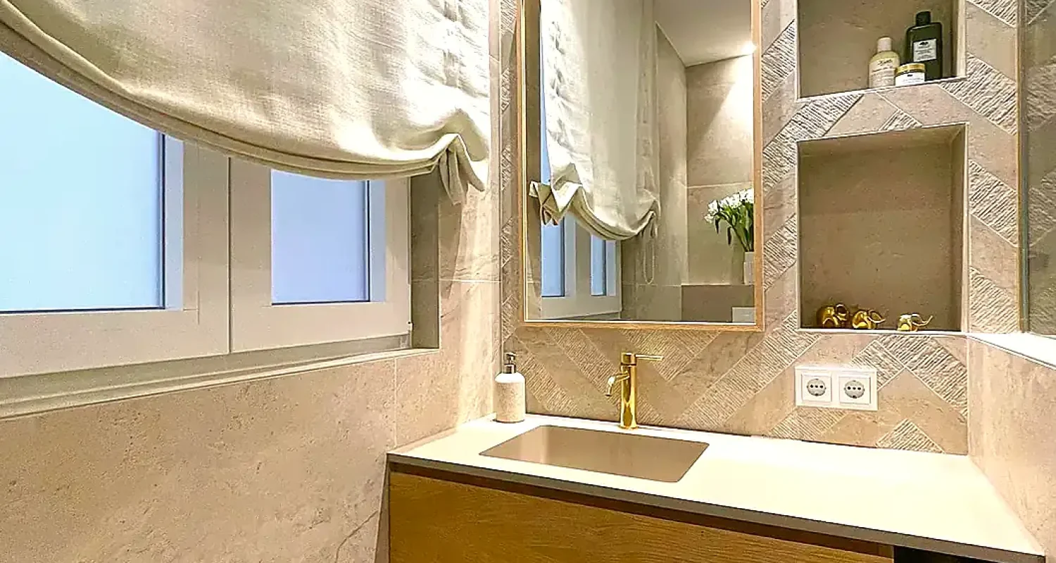 Baño de la reforma integral de piso en Alonso Cano, Madrid, con mueble de lavabo suspendido de madera, espejo dorado y revestimiento porcelánico.