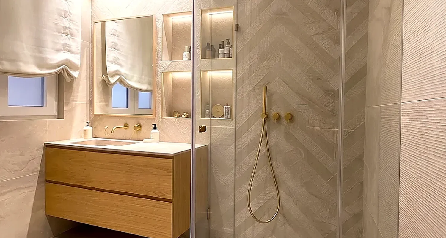 Baño reformado en calle Alonso Cano, Madrid, con ducha acristalada, mueble de lavabo suspendido de madera y revestimientos en tonos claros.