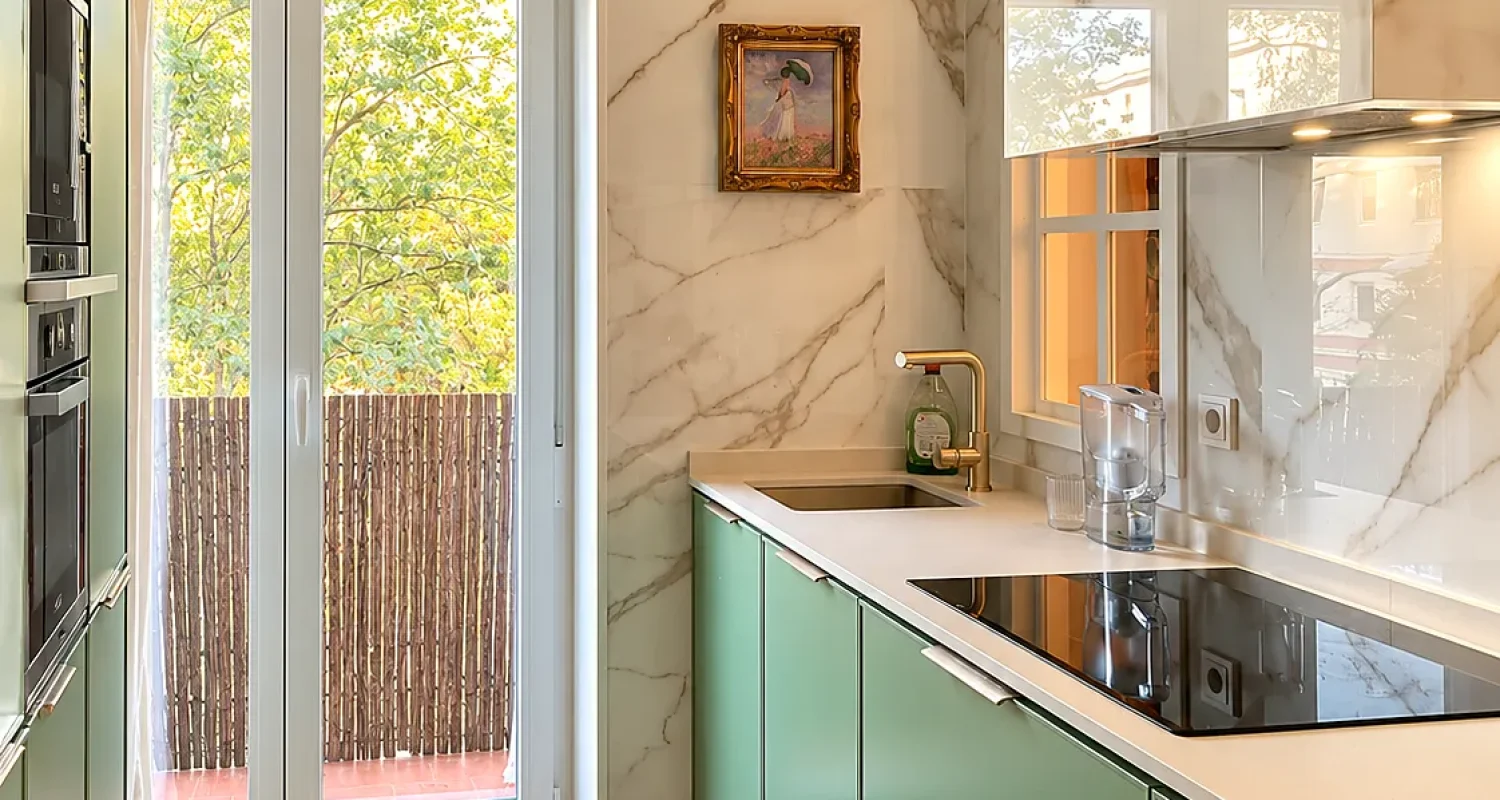 Cocina verde de la reforma integral de piso en Alonso Cano, Madrid, con muebles a medida, revestimiento efecto mármol y salida a terraza.
