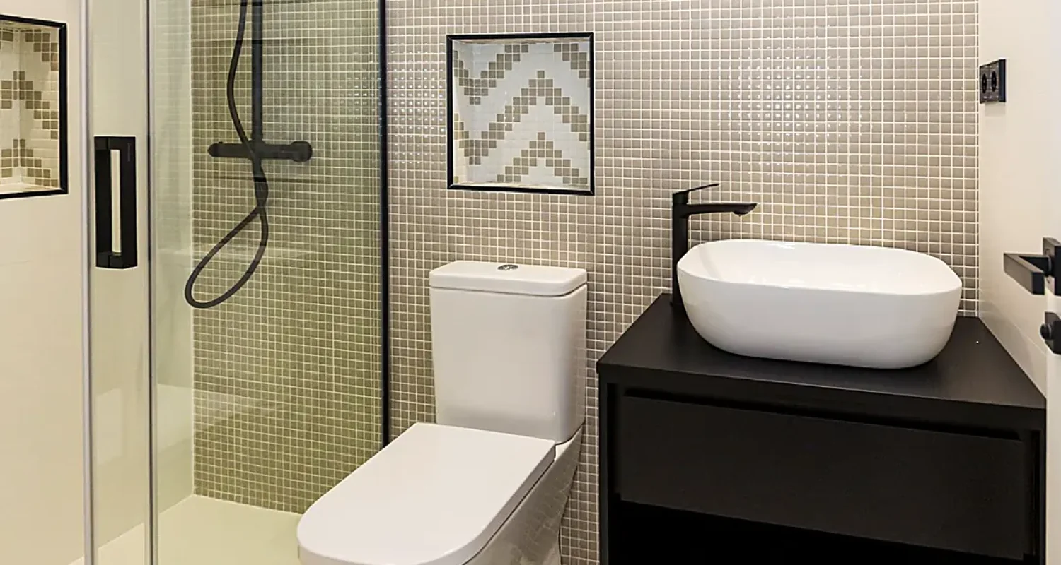 Baño reformado en calle Tarragona, Madrid, con mosaico geométrico, ducha con mampara de cristal y mueble de lavabo suspendido.