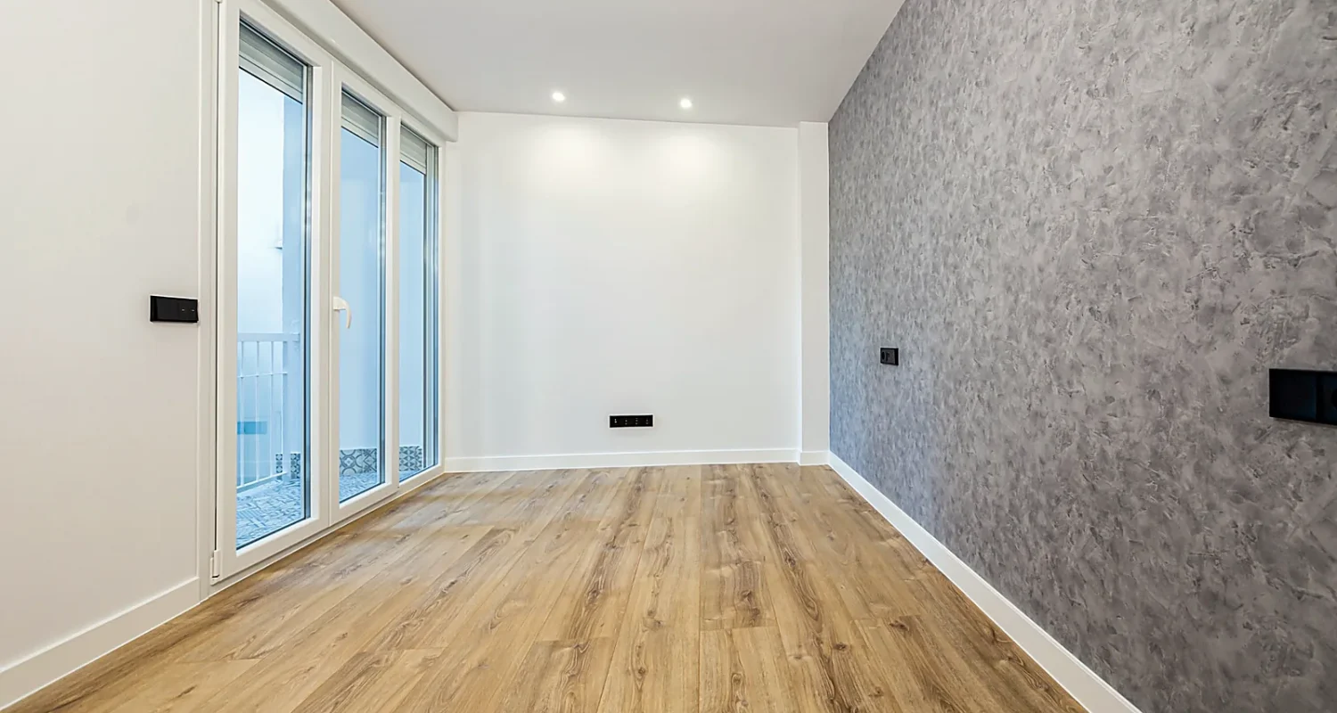 Habitación reformada en Calle Tarragona, Madrid, con pared gris texturizada, suelo de madera y paredes blancas