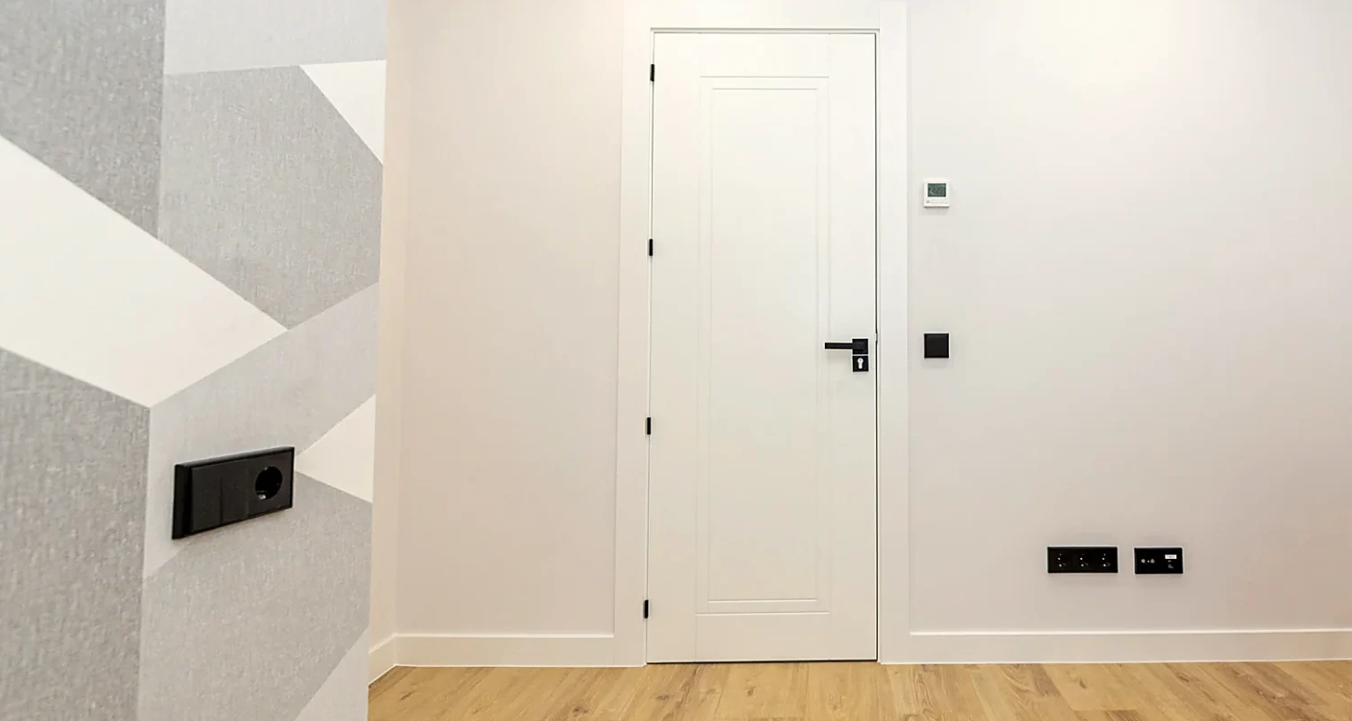 Habitación reformada en calle Tarragona, Madrid, con puerta blanca, pared decorativa geométrica y suelo efecto madera.
