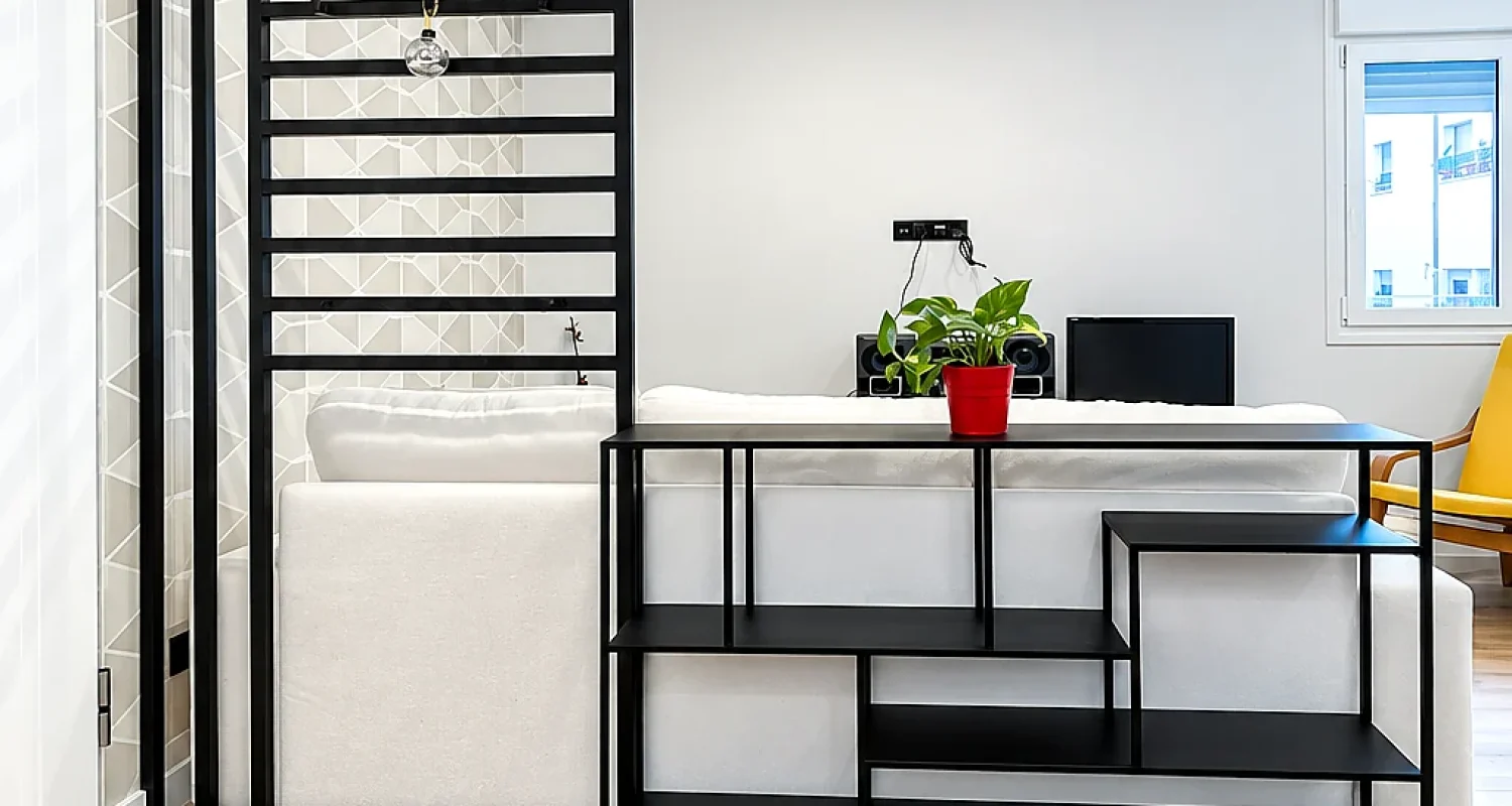 Salón reformado en calle Tarragona, Madrid, con separador metálico negro, sofá blanco y suelo de acabado madera.