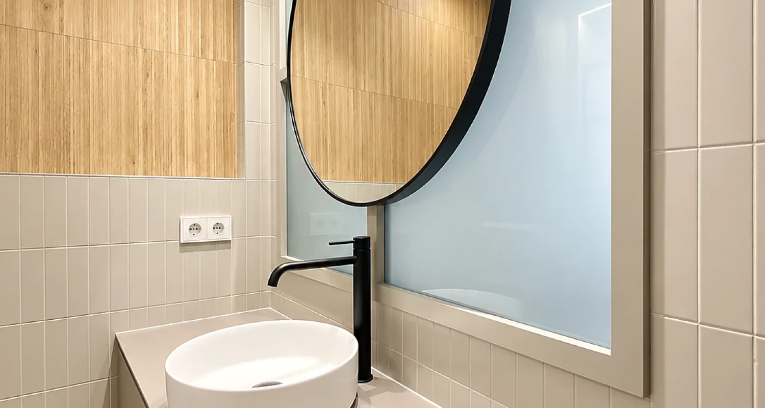Aseo reformado en chalet de Daganzo de Arriba con espejo circular negro, lavabo sobre encimera, grifería negra y revestimiento efecto madera.