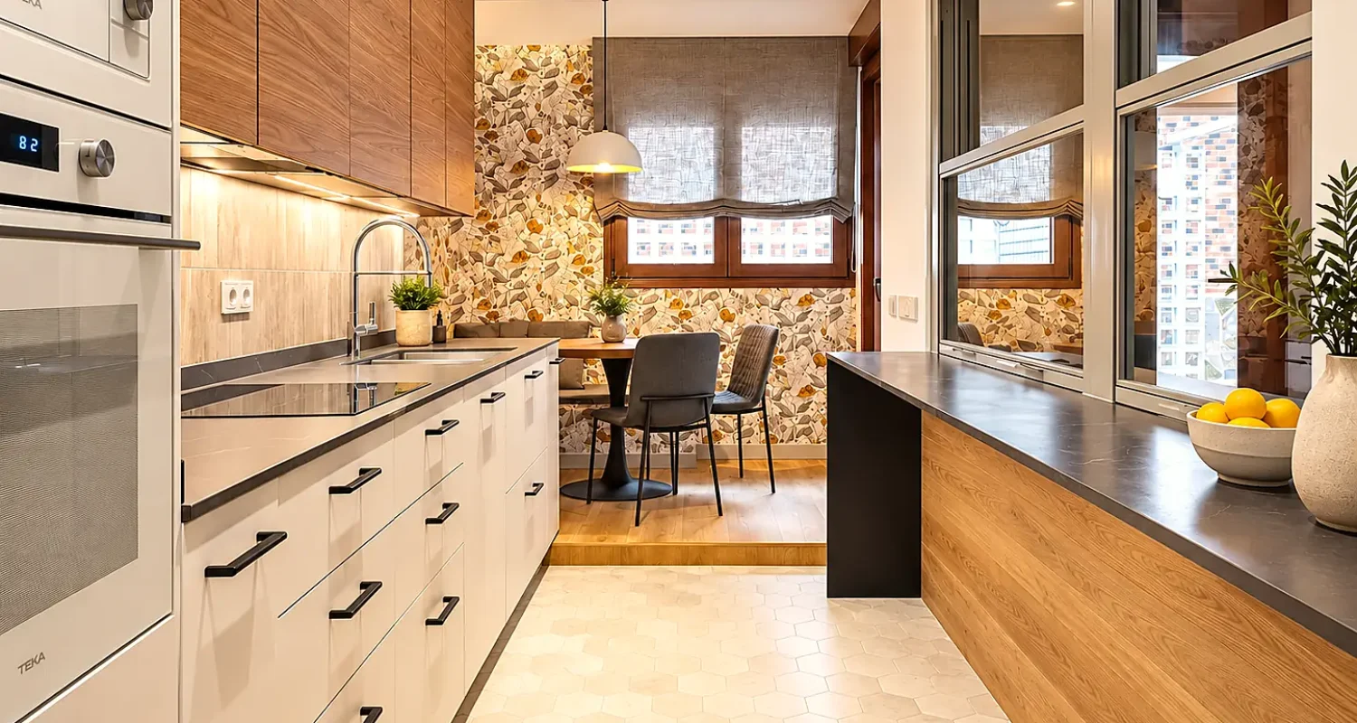 Cocina reformada en chalet de Daganzo de Arriba, con muebles blancos y de madera, encimera oscura y zona de comedor con papel pintado botánico.