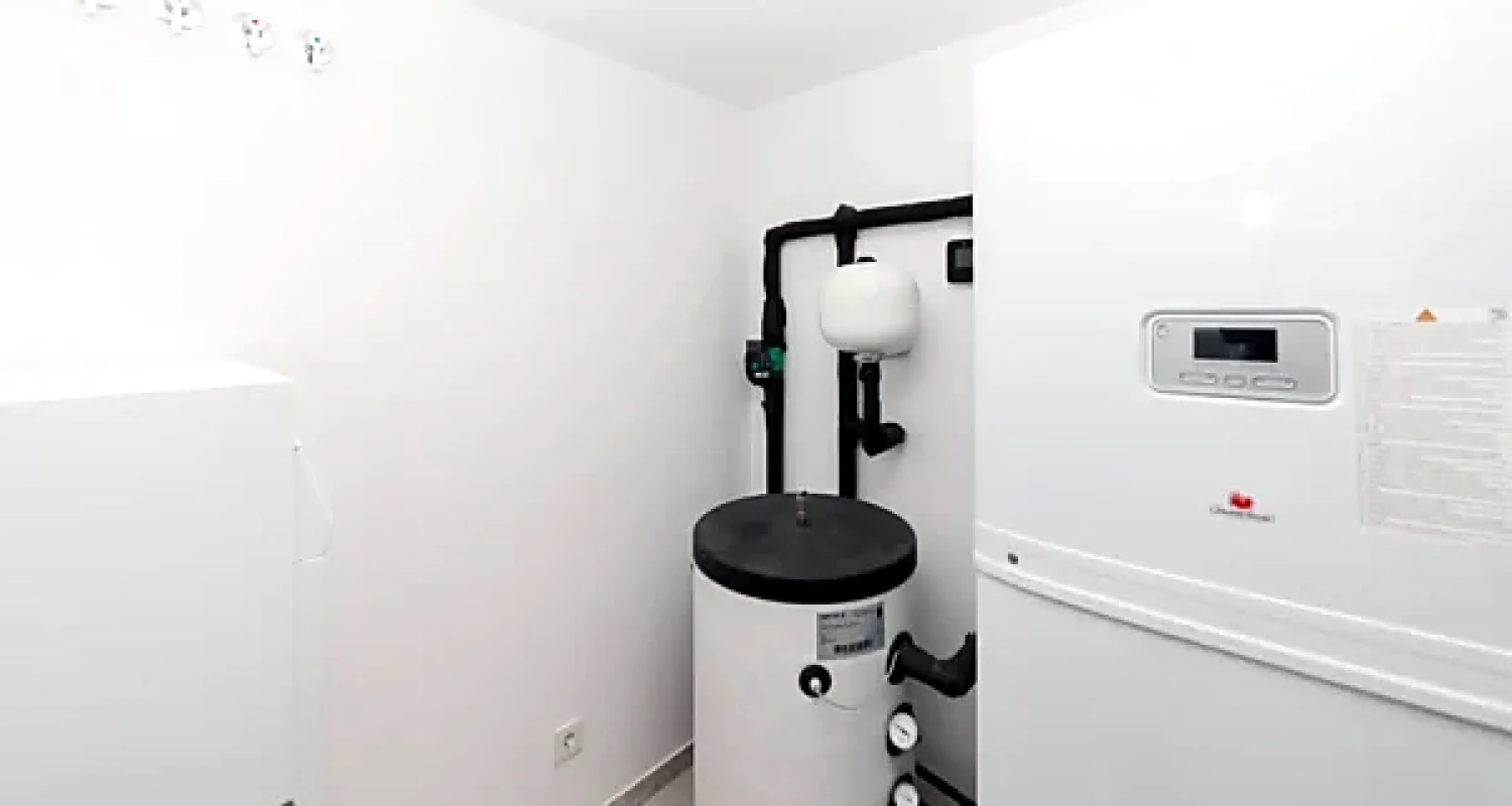 Cuarto técnico con equipos de aerotermia, depósito y tuberías aisladas en chalet reformado en Daganzo de Arriba, Madrid.