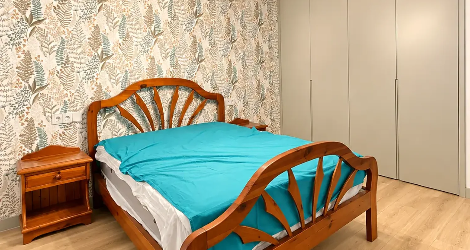 Dormitorio reformado en chalet de Daganzo con cama de madera, papel pintado botánico y ropa de cama turquesa.