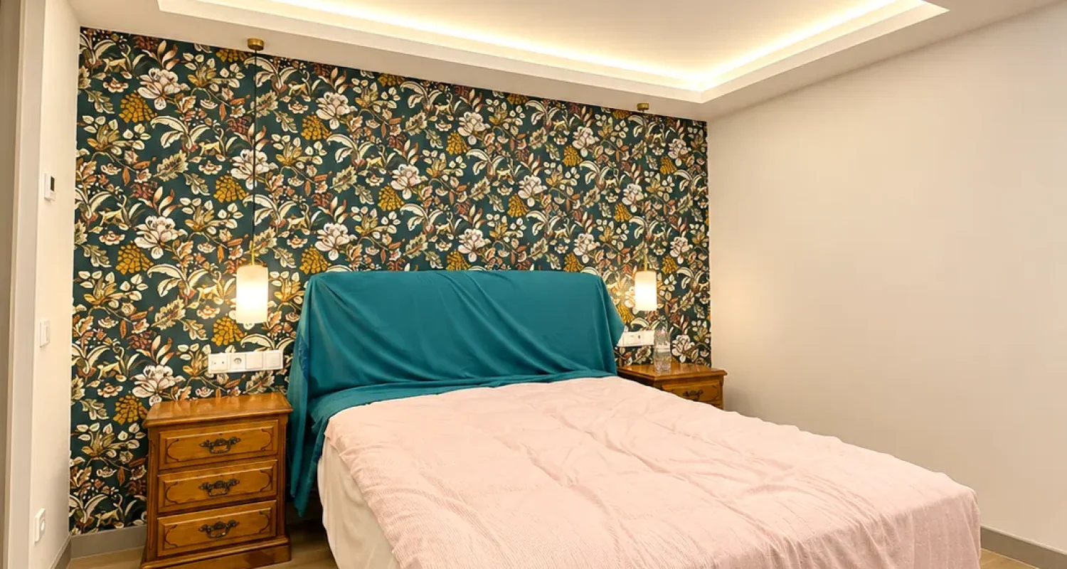 Dormitorio reformado en chalet de Daganzo de Arriba, con iluminación LED indirecta en el techo, papel pintado floral y suelo efecto madera.