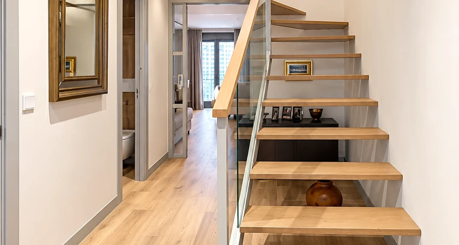Escalera interior con peldaños de madera y barandilla de cristal en reforma integral de chalet en Daganzo de Arriba, Madrid.