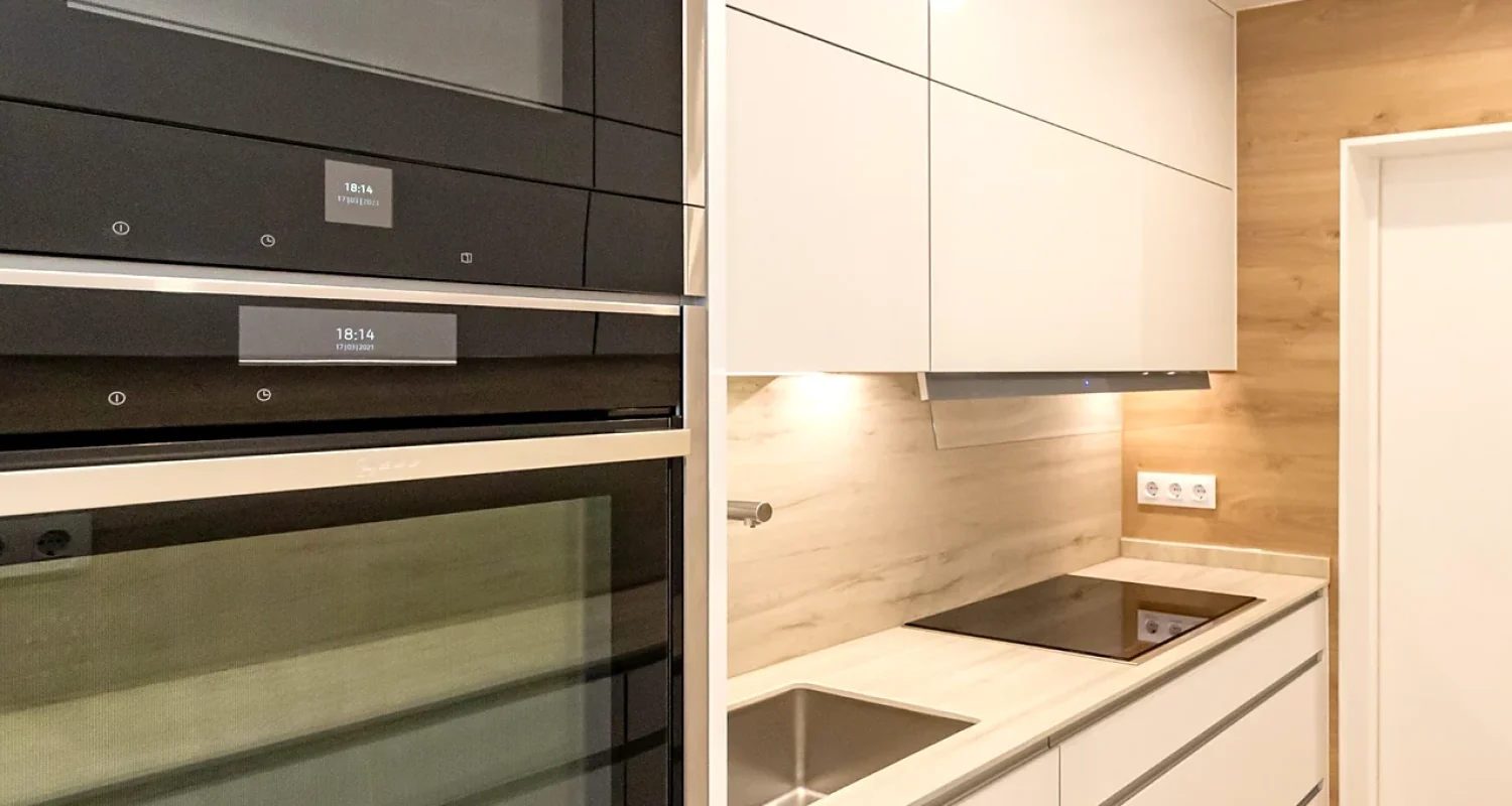 Cocina reformada en Mejorada del Campo, Madrid, con muebles blancos, horno integrado en columna y encimera clara.
