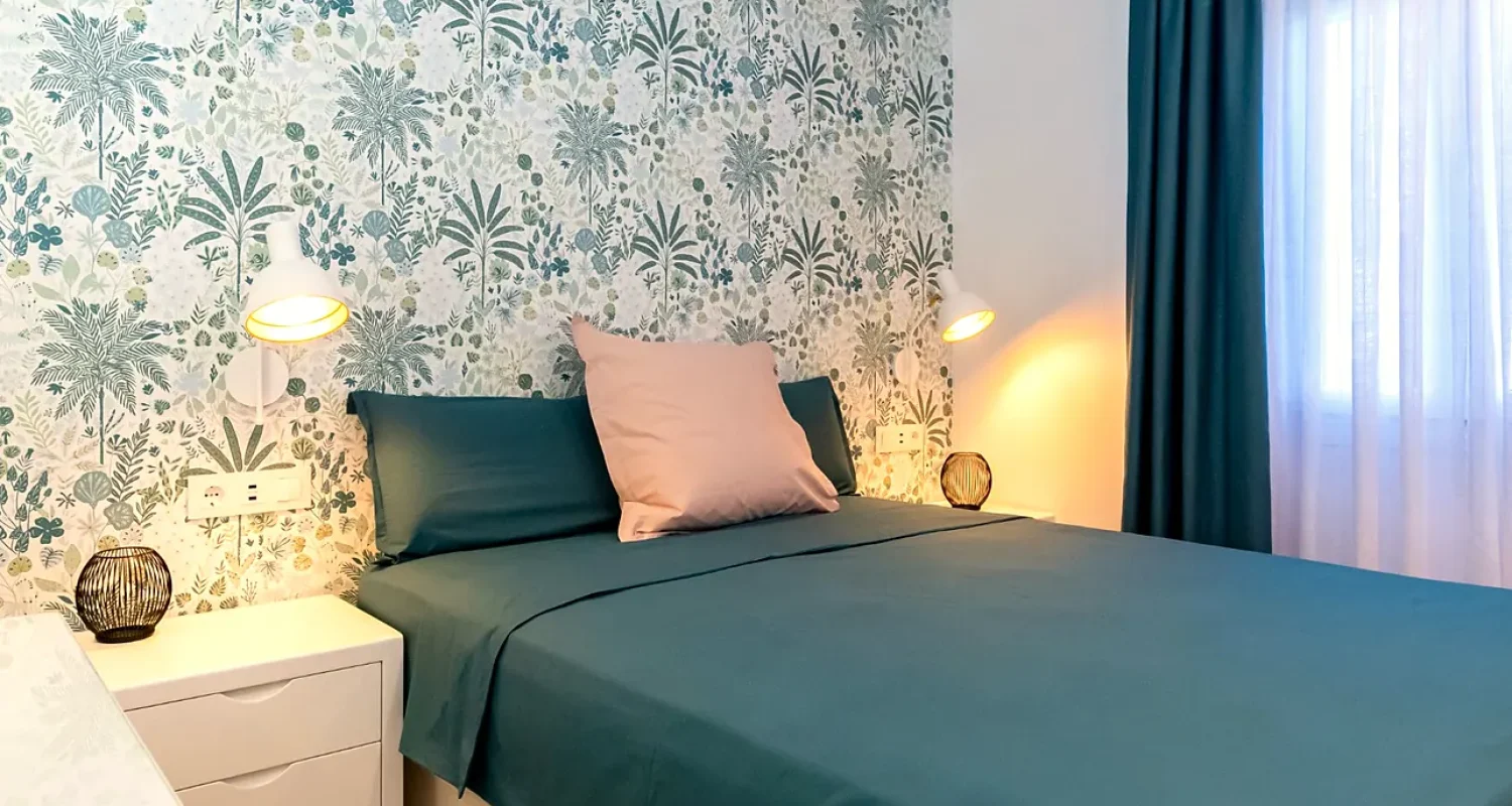 Dormitorio con cama doble azul, papel pintado decorativo y cortinas azules en vivienda reformada en Mejorada del Campo, Madrid.