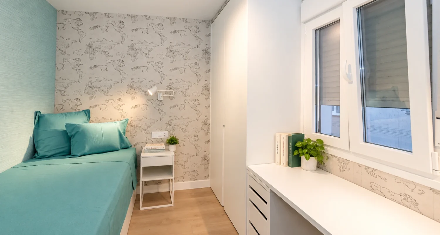 Dormitorio individual reformado en Mejorada del Campo con cama turquesa, armario blanco y escritorio junto a la ventana.