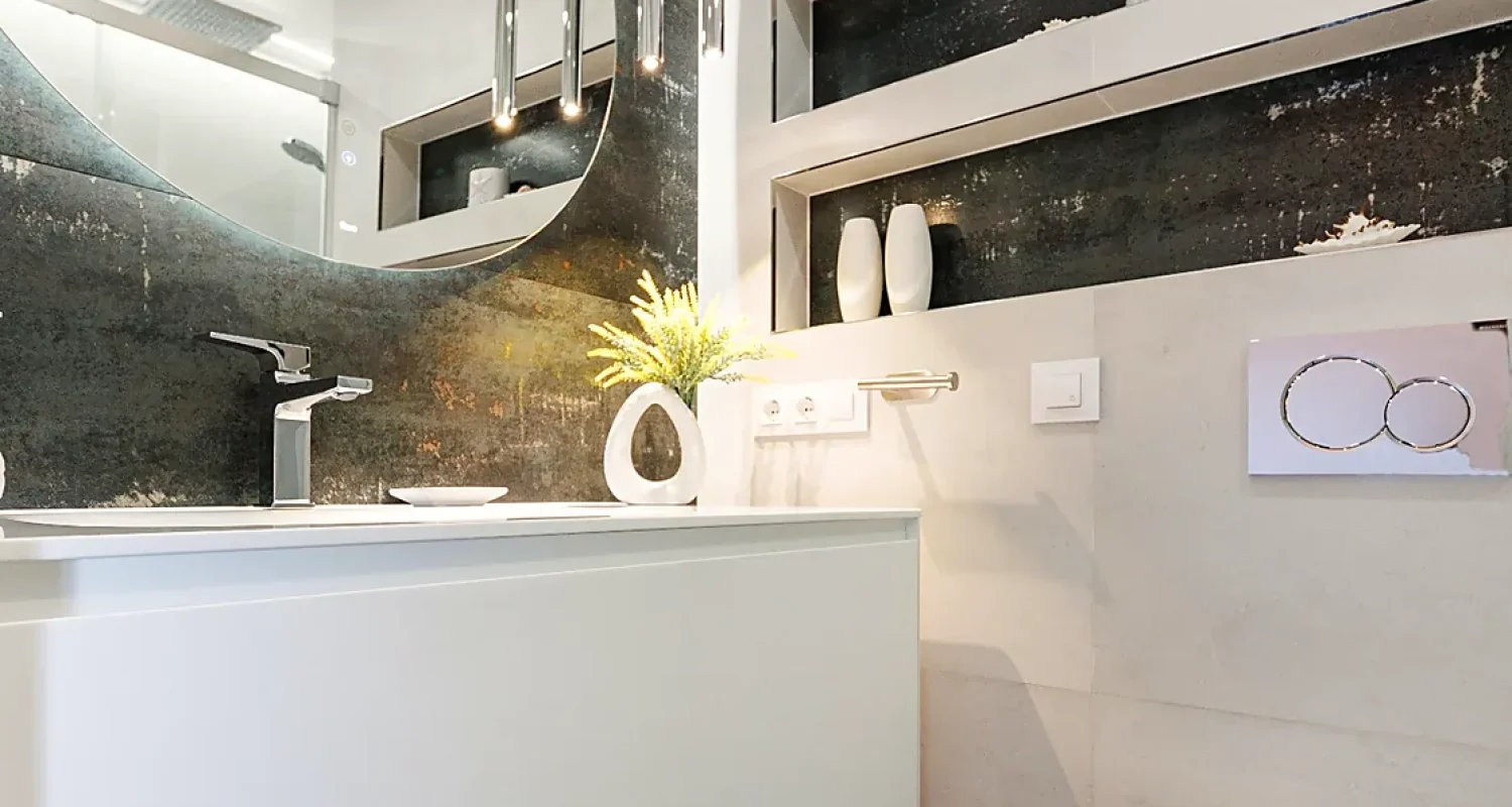 Baño reformado en Mejorada del Campo, Madrid, con lavabo sobre mueble suspendido blanco, espejo y revestimiento gris.