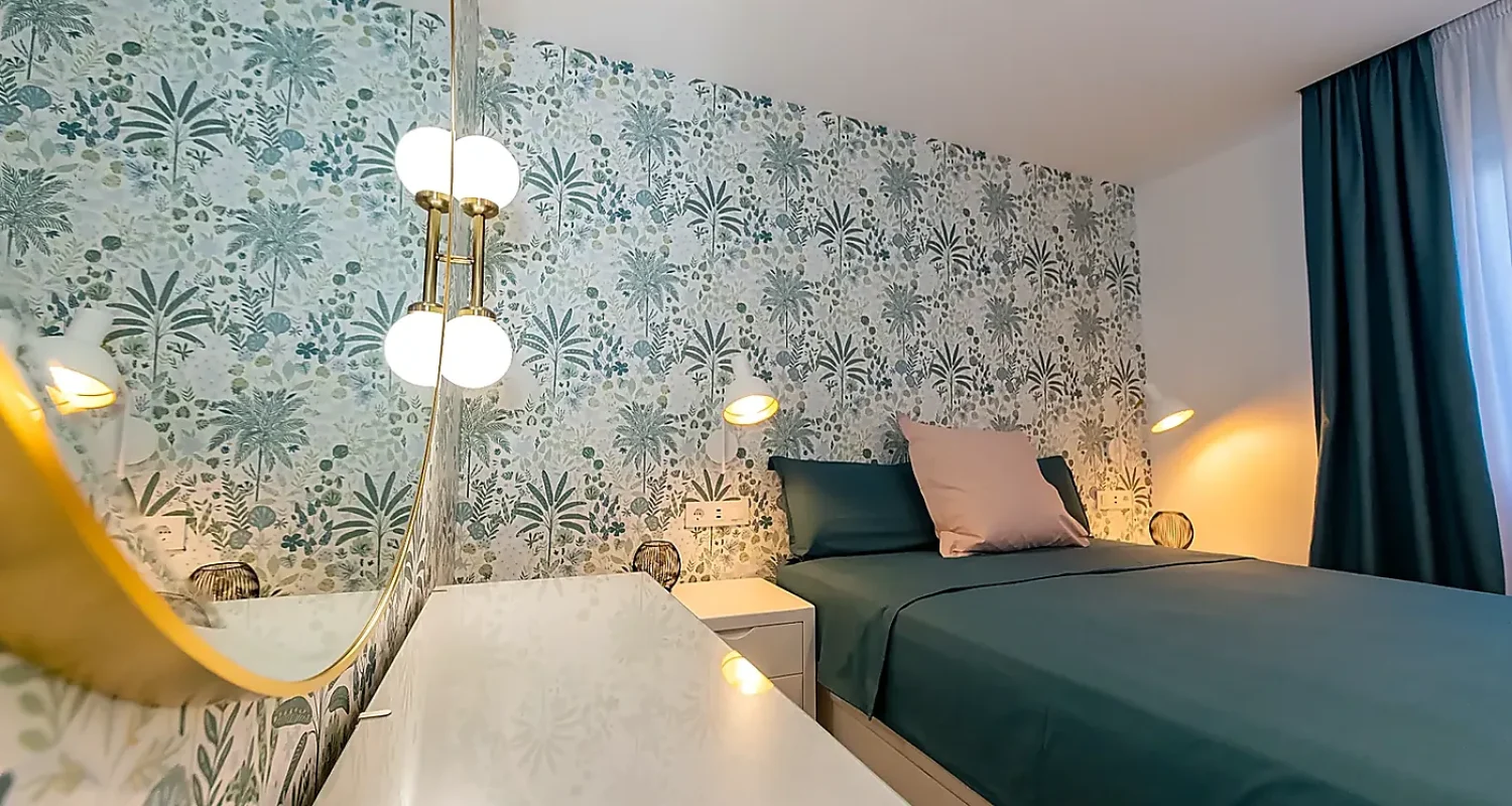 Dormitorio reformado en Mejorada del Campo, Madrid, con espejo dorado, cómoda blanca, pared decorativa y cama azul.