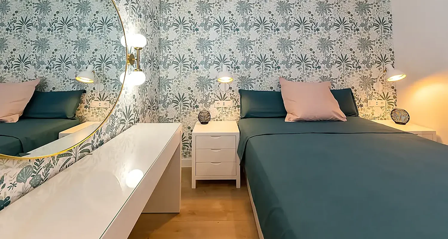 Dormitorio reformado en Mejorada del Campo, Madrid, con papel pintado botánico, cama azul verdosa y mobiliario blanco.