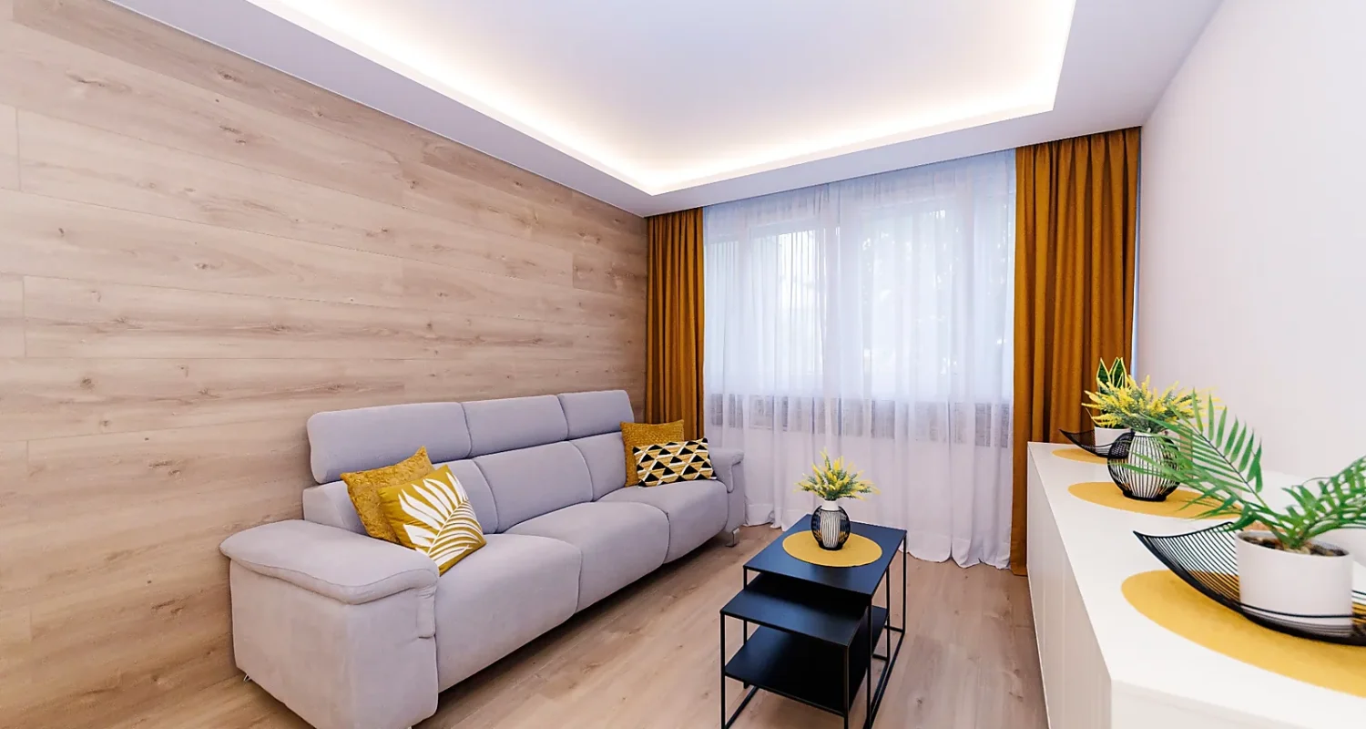Salón de piso reformado en Mejorada del Campo, Madrid, con sofá gris, panel de madera e iluminación LED indirecta.